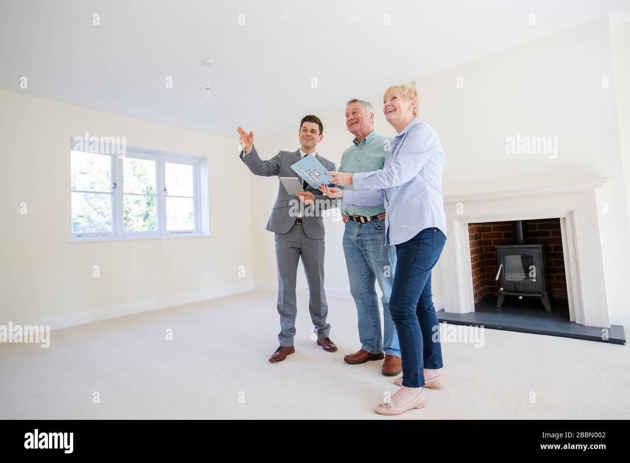 Realtor With Digital Tablet Showing Senior Couple Looking To Downsize Around Retirement Home Stock Photo
