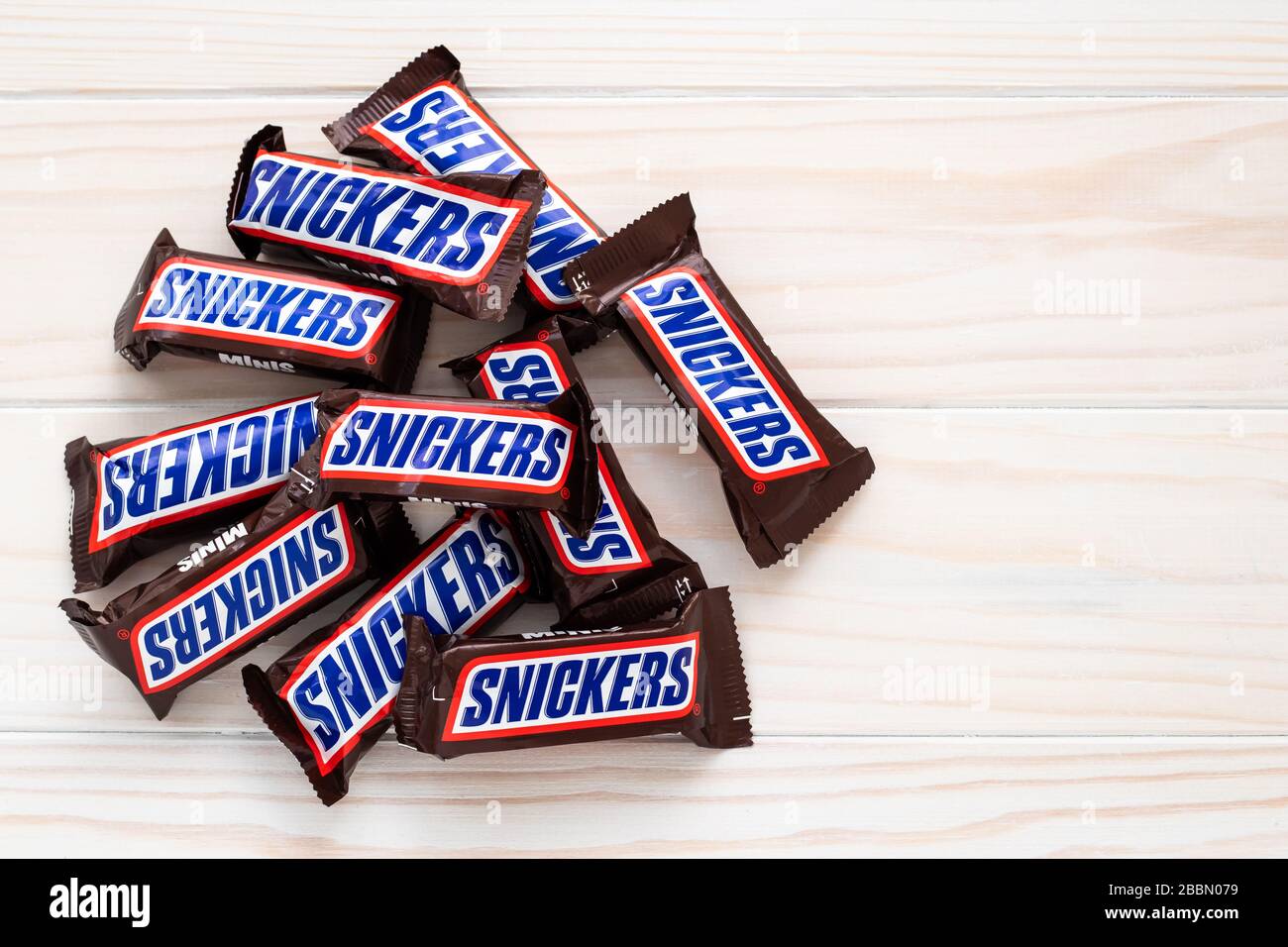 Kharkov, Ukraine, April 01, 2020: Heap of bars of snickers in wrapper on light wooden background. Illustrative editorial Stock Photo