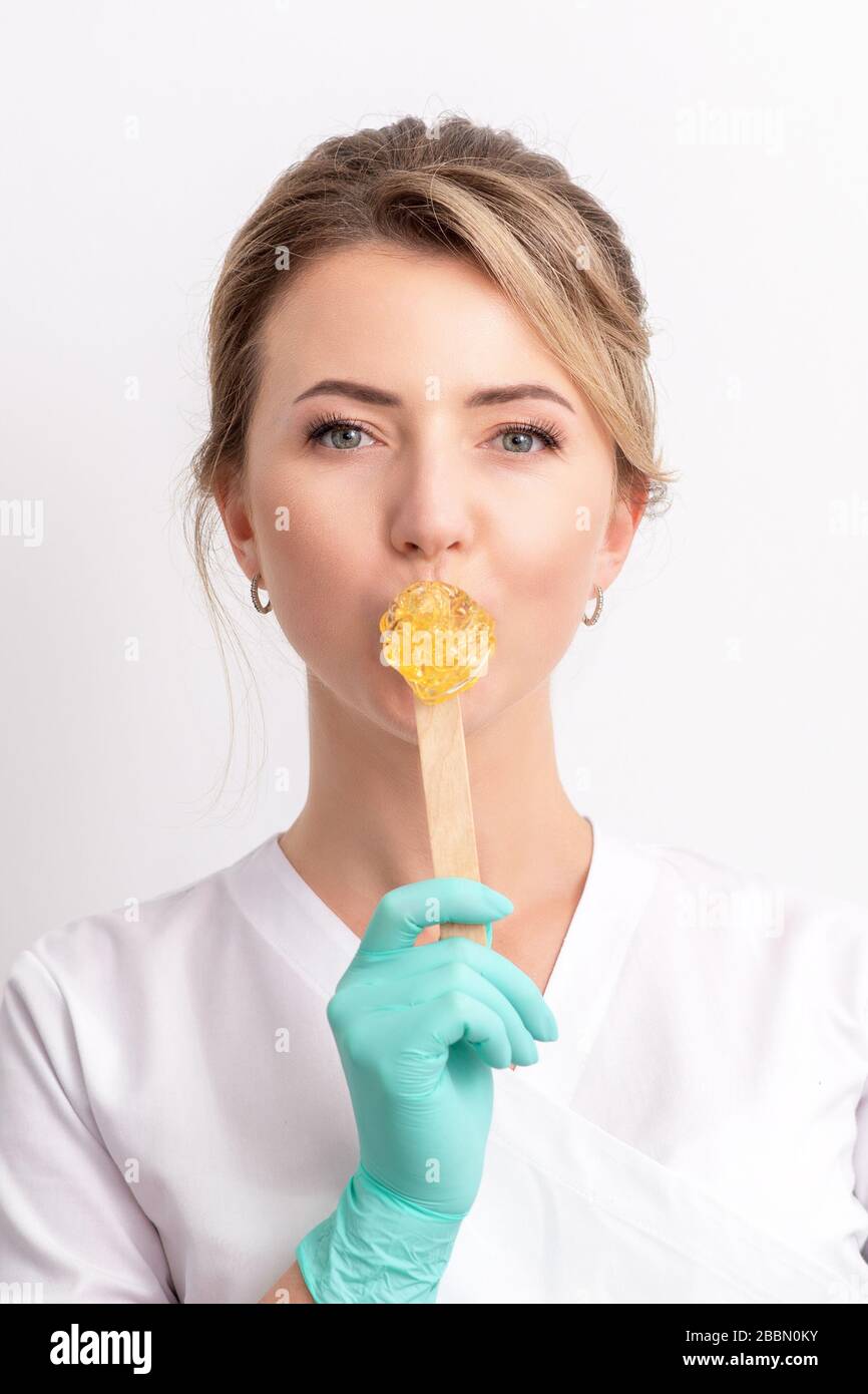 Beautician holds stick with wax while covering her lips on white