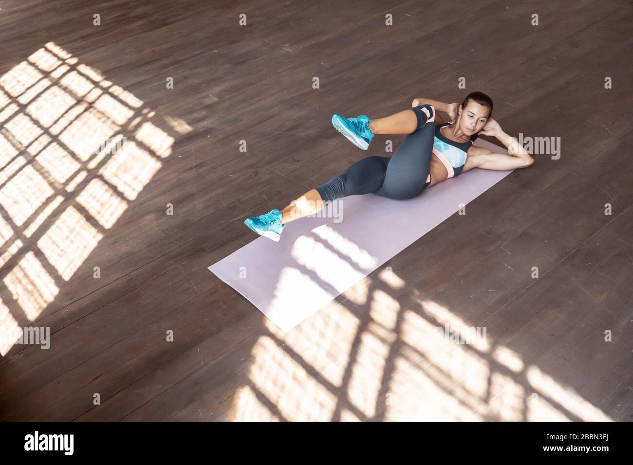 Sporty fit woman doing bicycle crunch exercise lying on mat in gym, top view. Stock Photo