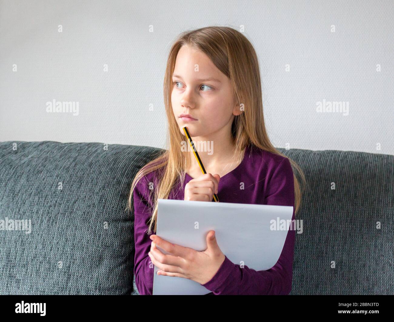 A girl is sitting on a couch and is thinking about what to write with a pencil on paper notes Stock Photo