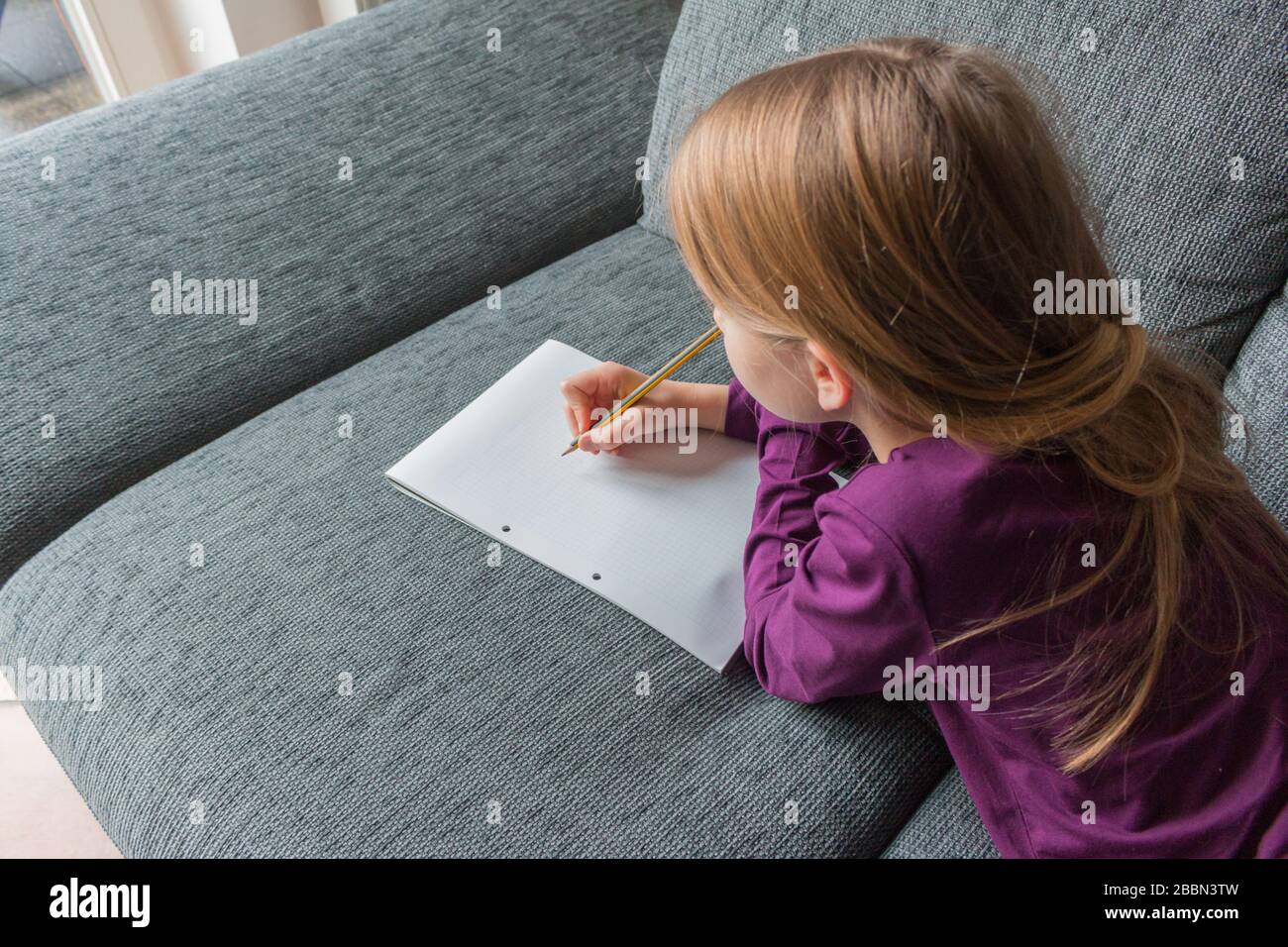 A girl is lying on a couch and is writing with a pencil on paper notes Stock Photo