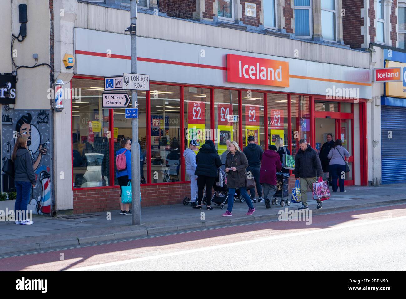 People standing two meters apart or social distancing whilst queuing to buy food at an Iceland supermarket Stock Photo