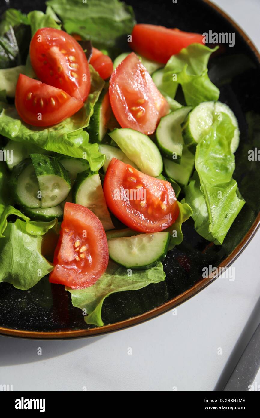 Summer fresh detox salad with tomatoes, cucumber, romaine lettuce and olive oil on marble background. Healthy diet food for vegan or vegetarian, top v Stock Photo
