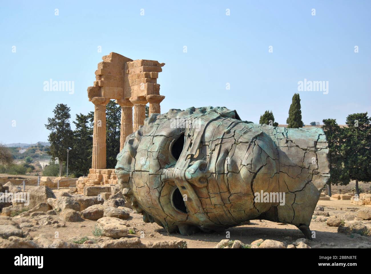 Fallen ancient Greek sculpture head fallen in front of the remains of a Greek temple at Valley of Temples at Agrigento (Sicily, Italy) Stock Photo