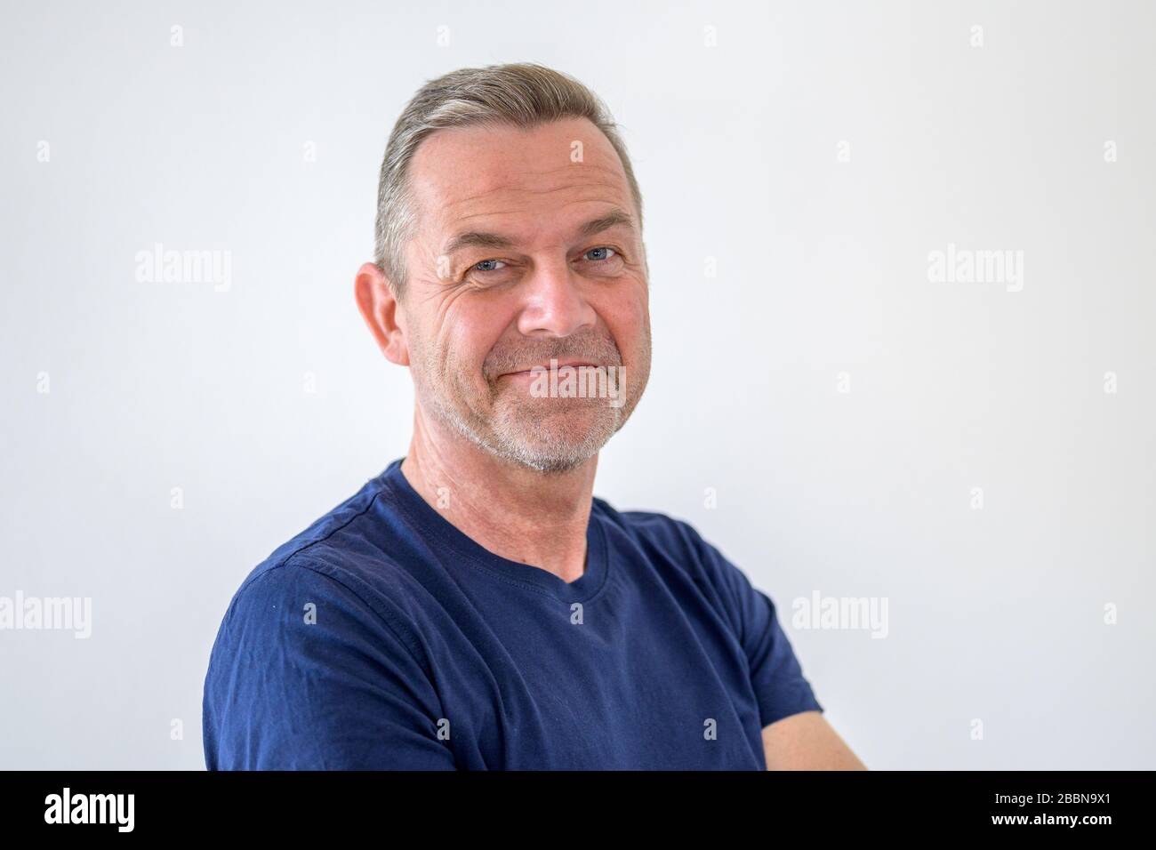 Smiling friendly attractive middle-aged man in casual blue T-shirt in a head and shoulders portrait on white with copy space Stock Photo