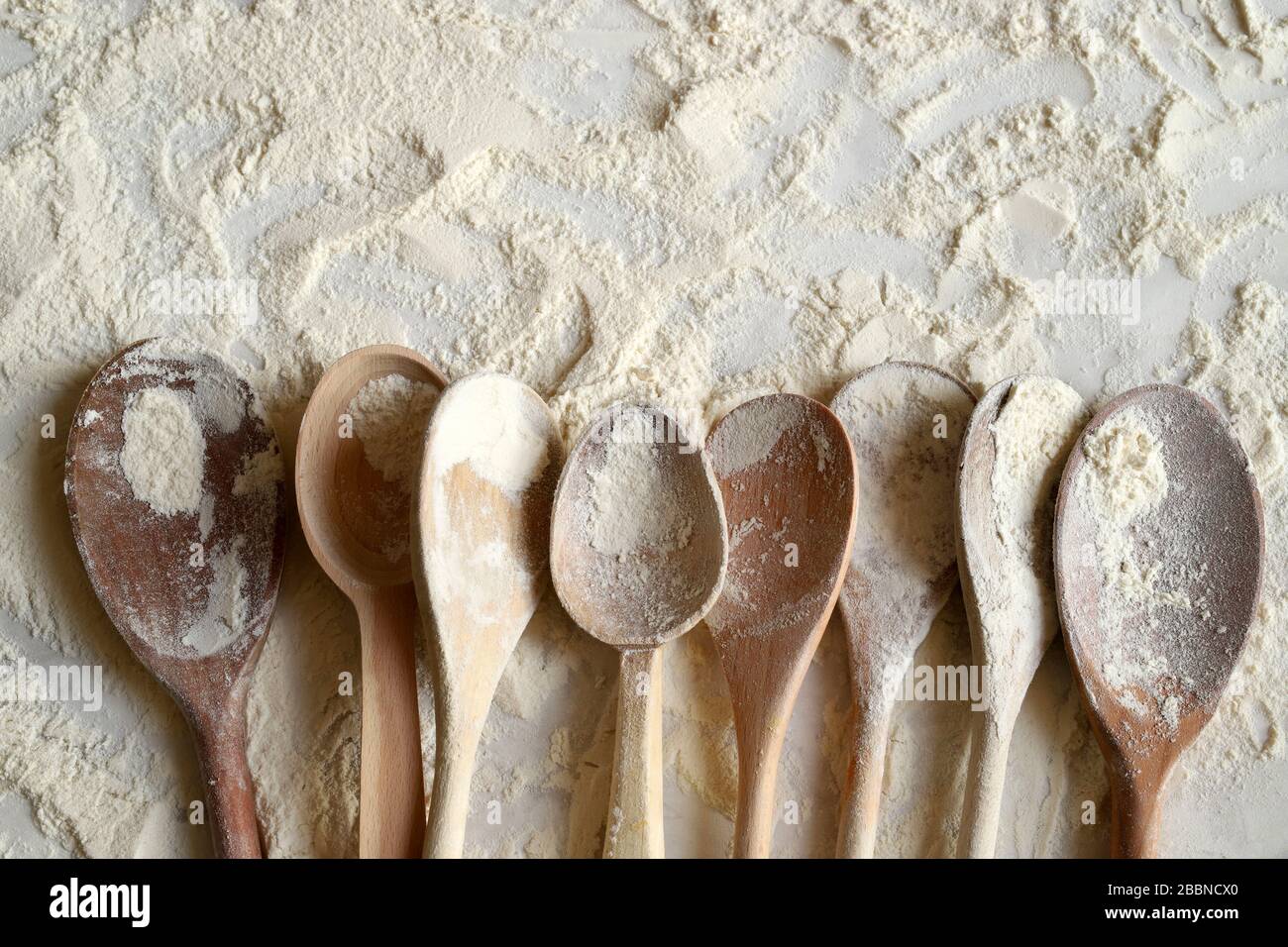 Baking concept. Top view of wooden spoons sprinkled with wheat flour on ...