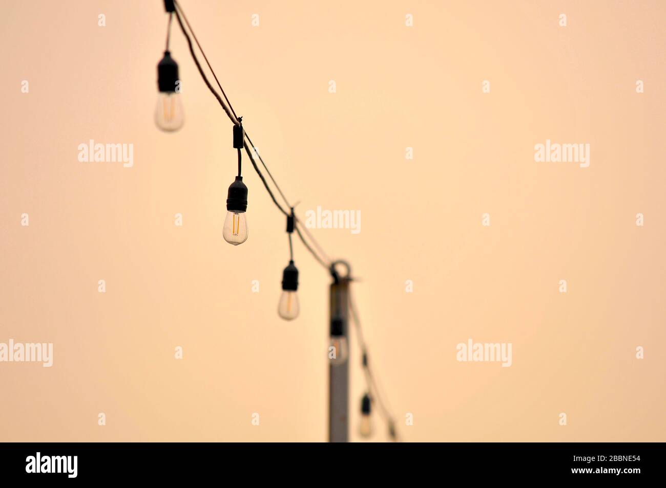 String of electric light bulbs on a pale orange sky background Stock Photo
