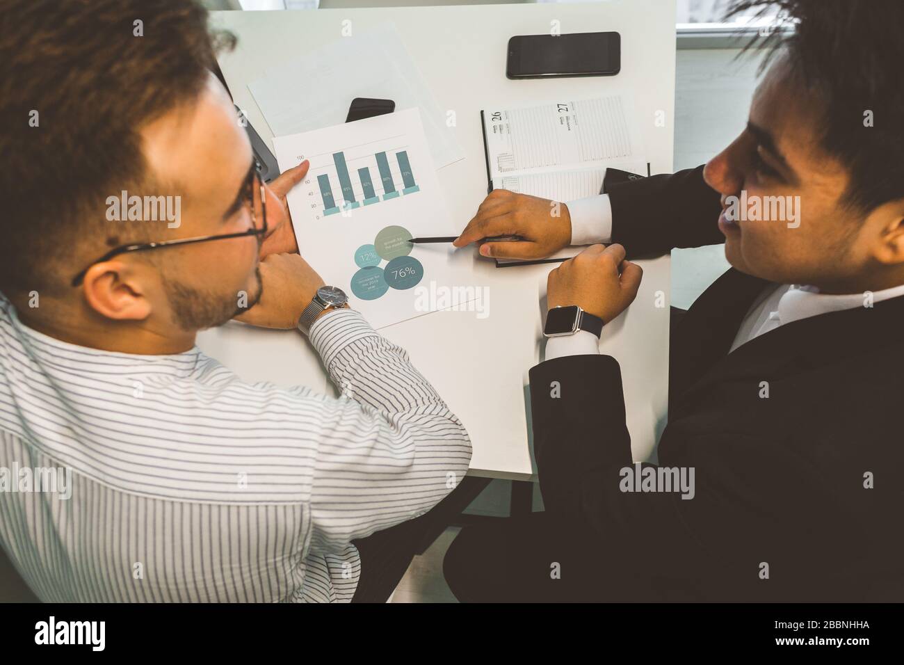 Young office worker sitting at desk, using computer. Two business man talking Stock Photo