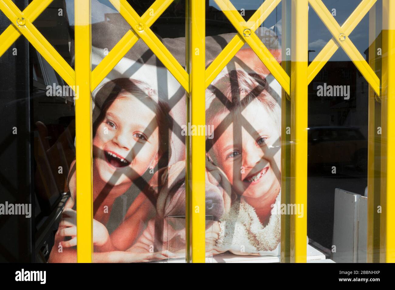 As the second week of the Coronavirus lockdown continues around the capital, and the UK death toll rising by 563 to 2,325, with 800,000 reported cases of Covid-19 worldwide, two young girls smile with their pet dog on a printed cushion in the window of a Snappy Snaps shop in Clapham - a metaphor for family isolation and social distancing during the pandemic, on 1st April 2020, in London, England. Stock Photo