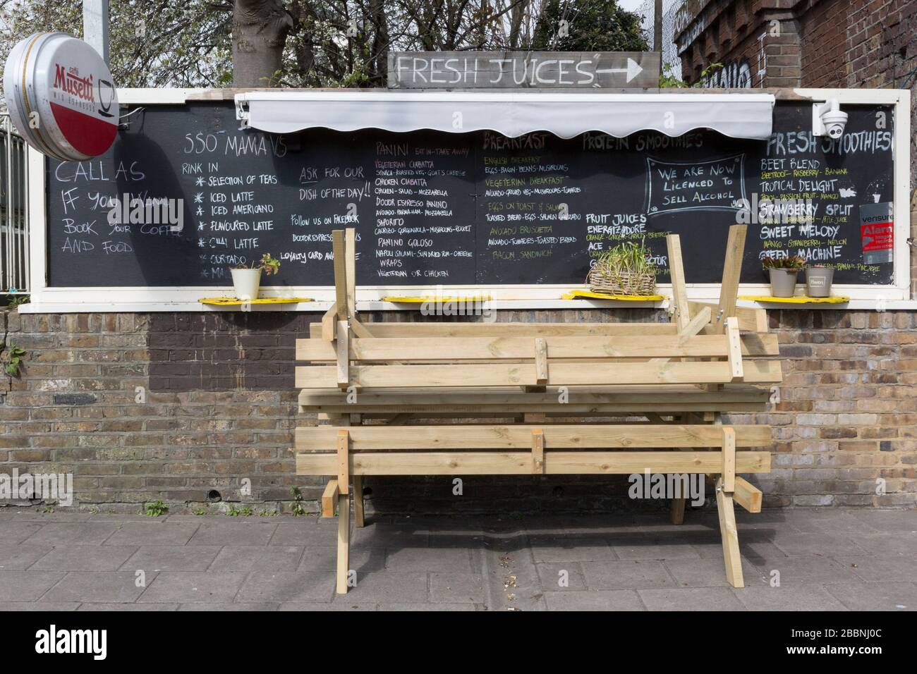 As the second week of the Coronavirus lockdown continues around the capital, and the UK death toll rising by 563 to 2,325, with 800,000 reported cases of Covid-19 worldwide, in accordance with the government's forced lockdown and closure of businesses, benches are upturned in front of daily menu for drinks and food snacks outside a cafe near the local Overground station on Clapham High Street, on 1st April 2020, in south London, England. Stock Photo