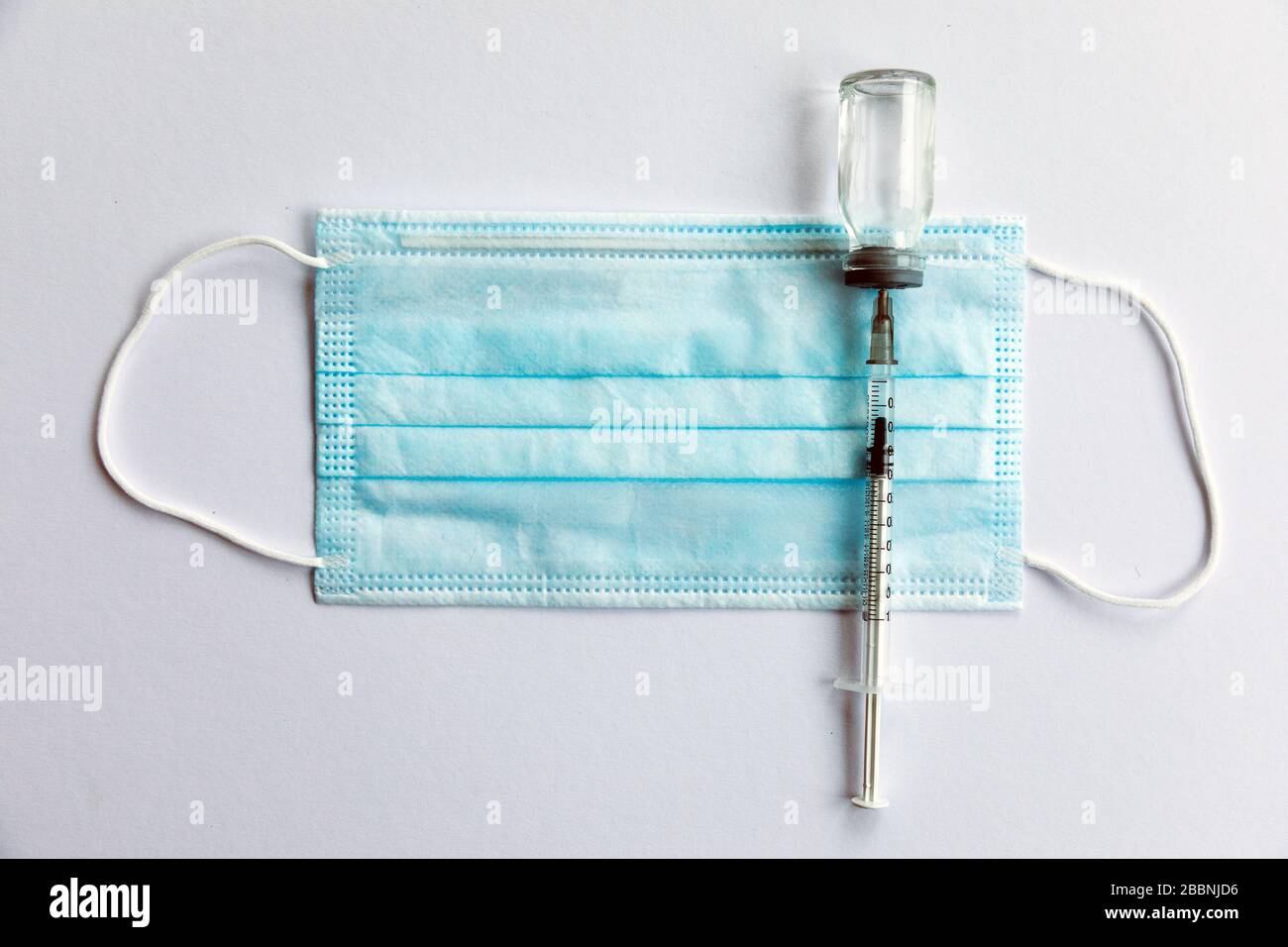 Disposable medical syringe, vaccine ampoule, protective mask. White background. Stock Photo