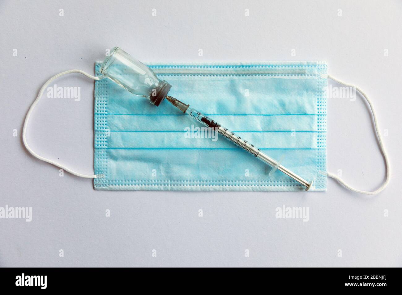 Disposable medical syringe, vaccine ampoule, protective mask. White background. Stock Photo