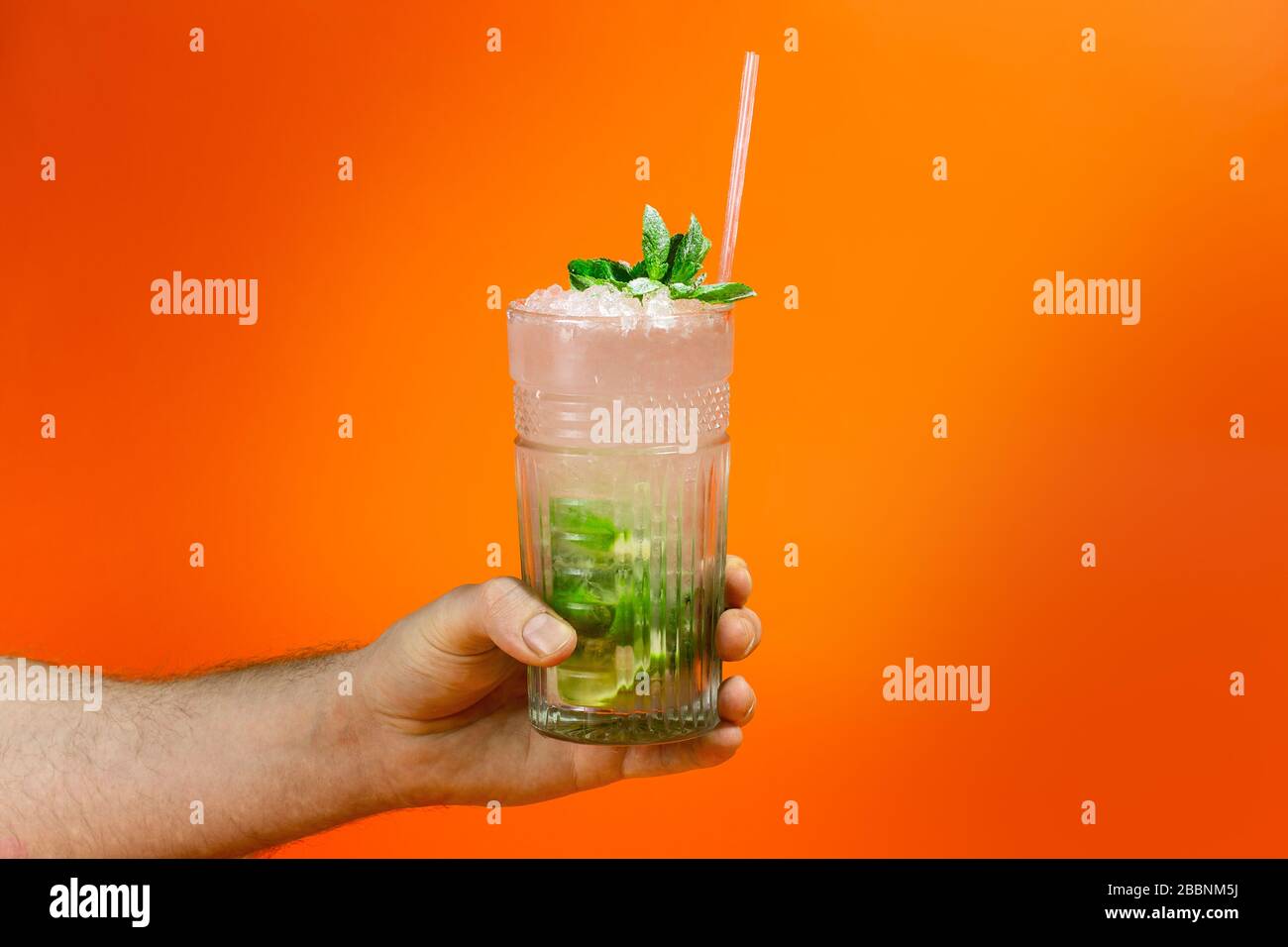https://c8.alamy.com/comp/2BBNM5J/close-up-of-a-mans-hand-holding-a-glass-of-tropical-mojito-cocktail-on-orange-background-with-copy-space-summer-time-vacation-concept-2BBNM5J.jpg