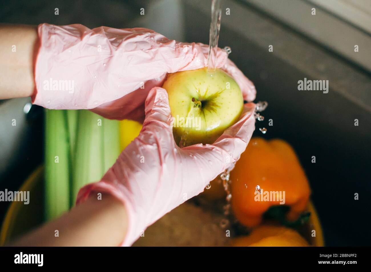 Washing fruits. Hands in pink gloves washing apple in water stream in