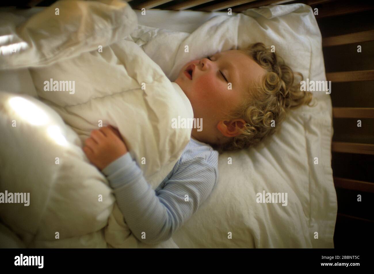 A kid covered by a bedspread sleeping comfortably. Stock Photo