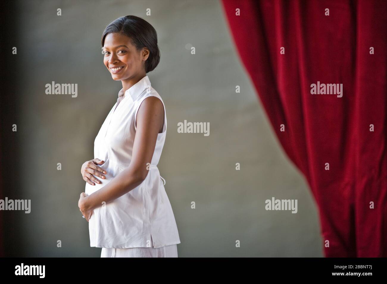 Portrait of a smiling pregnant mid-adult woman standing with her hand on her belly. Stock Photo