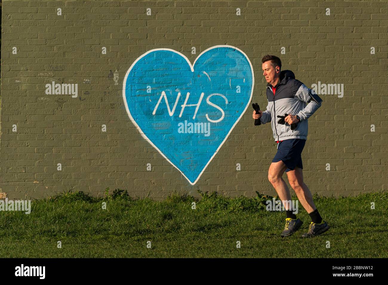 © 2020 Andrew Baker 24th March 2020. Morning runner on the Wanstead flats run past graffiti supporting the NHS. Photograph © Andrew Baker Stock Photo