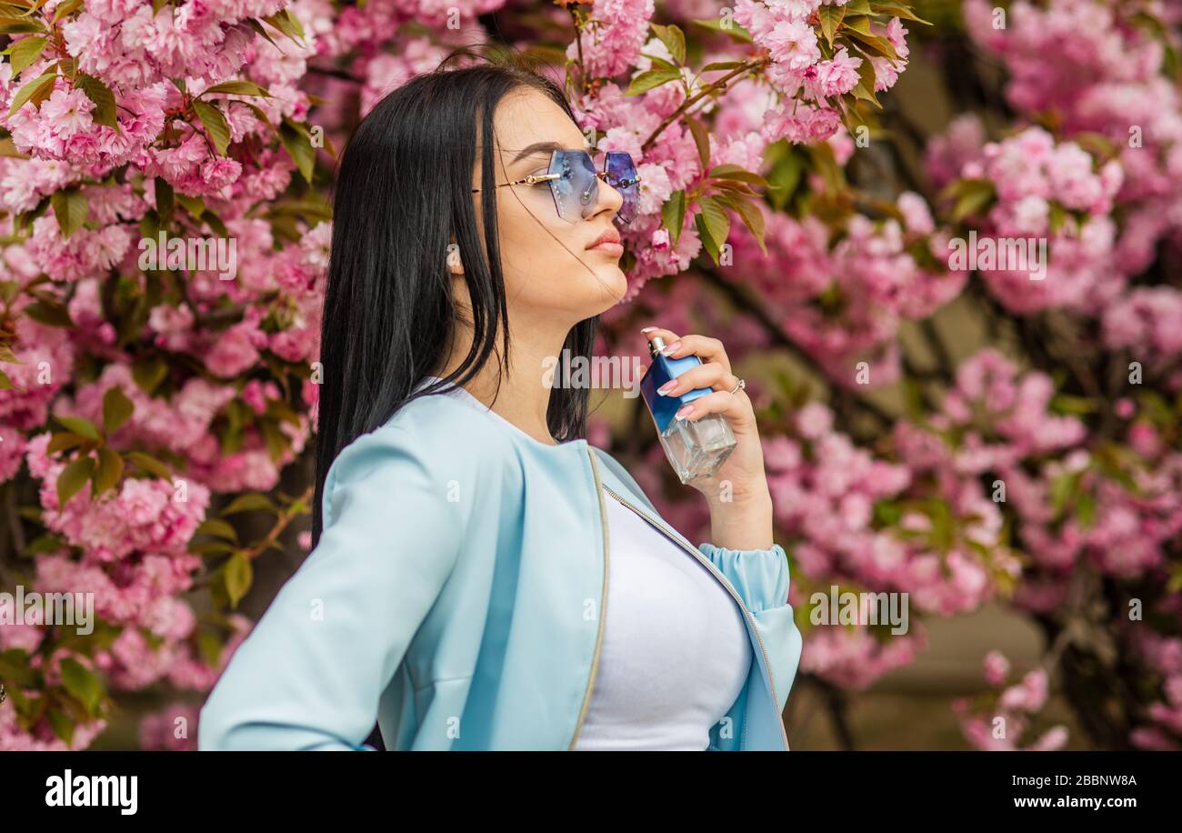 Cherry blossom aroma. Fashionable woman hold perfume bottle. Female perfume. Spring perfume. Fancy style. Aromatic compounds. Natural fragrant essential oils. Eau de Toilette. Luxury fragrance. Stock Photo