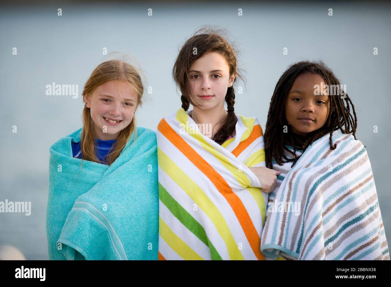 Portrait of three girls standing on a jetty wearing towels. Stock Photo