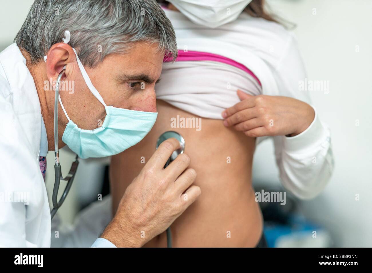 Doctor wearing mask with stethoscope visiting young girl in coronavirus times. Stock Photo
