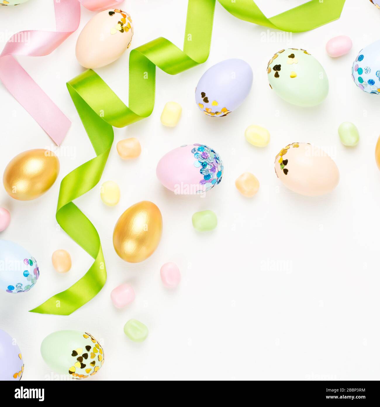 Festive Easter background with decorated eggs, flowers, candy and ribbons in pastel colors on white background Stock Photo