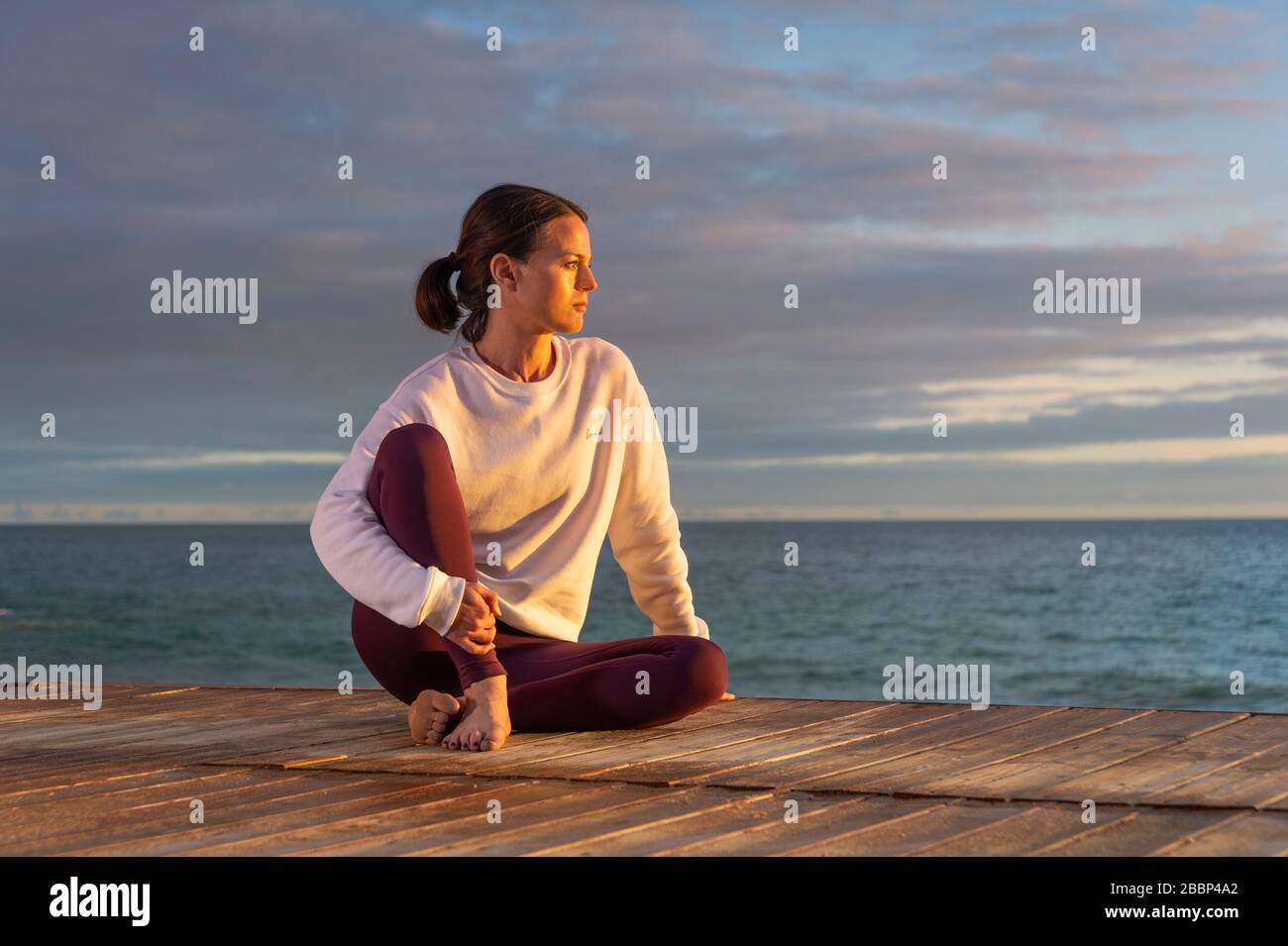 sporty woman sitting by the ocean at sunset, alone, thinking, Stock Photo