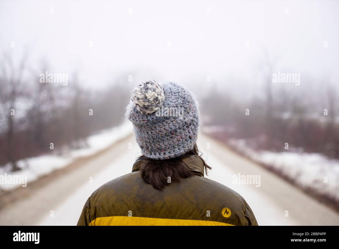 A lady walks alone on a gravel road during the emergency regulations regarding the coronavirus / COVID-19, on a foggy cold spring day. Stock Photo