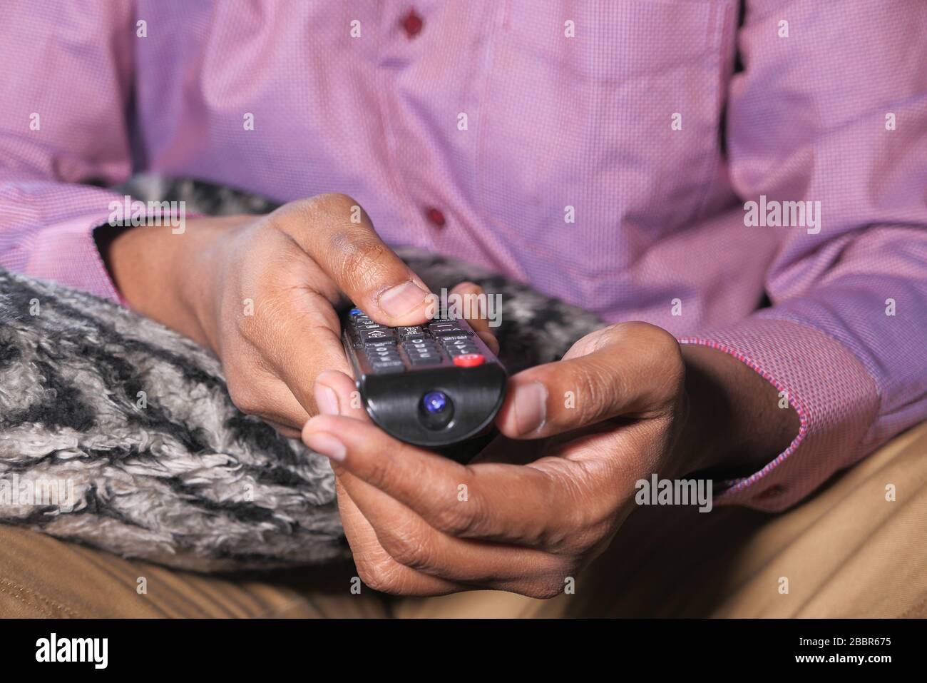 Hand holding remote control sitting on sofa . Stock Photo
