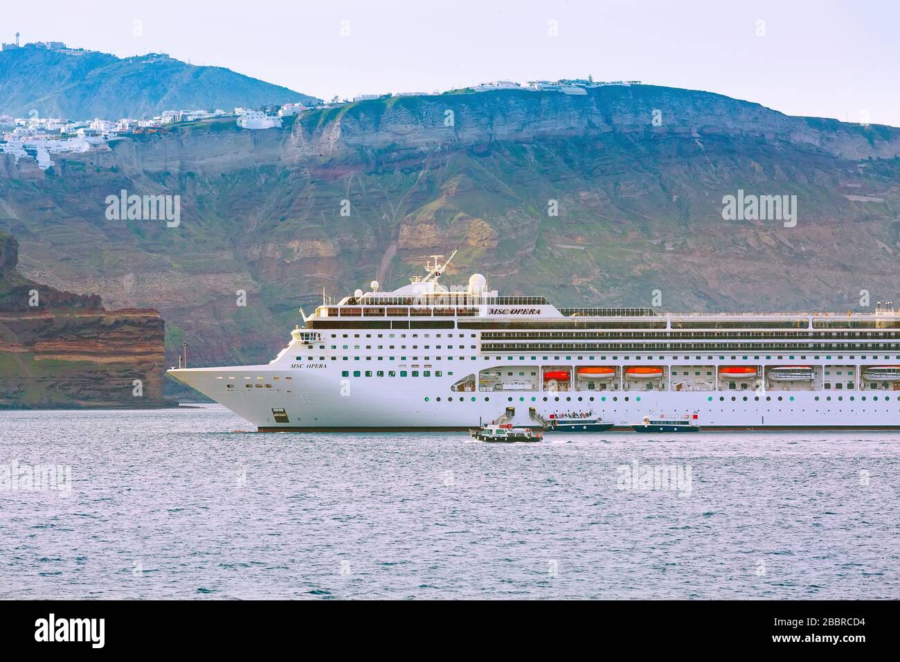 Oia, Santorini, Greece - April 25, 2019: Cruise ship MSC Opera, volcanic island shore and village panorama Stock Photo