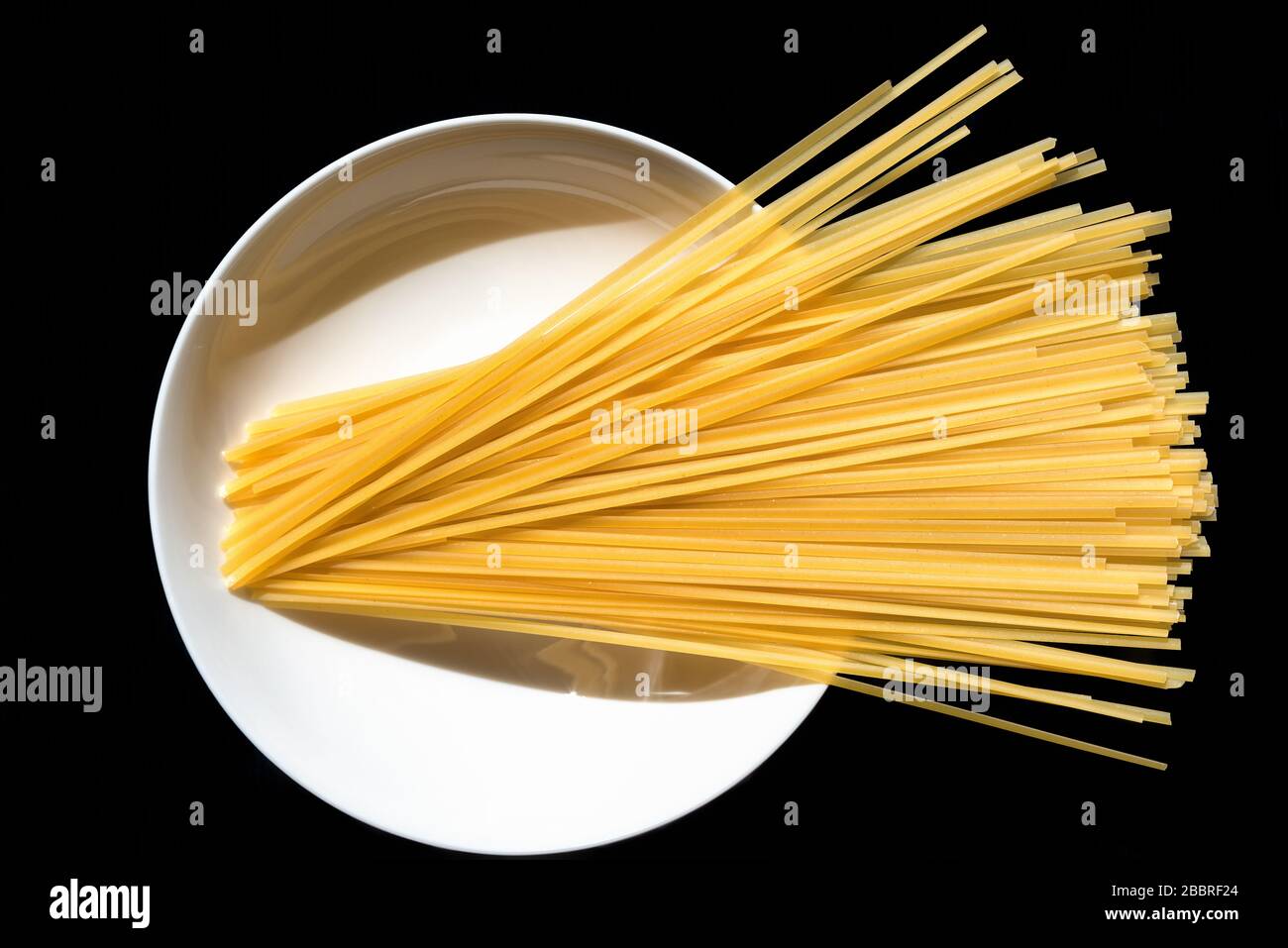 Original raw Italian pasta on a white  plate. Linguine ready to be cooked. Italian cuisine ingredient concept. Stock Photo
