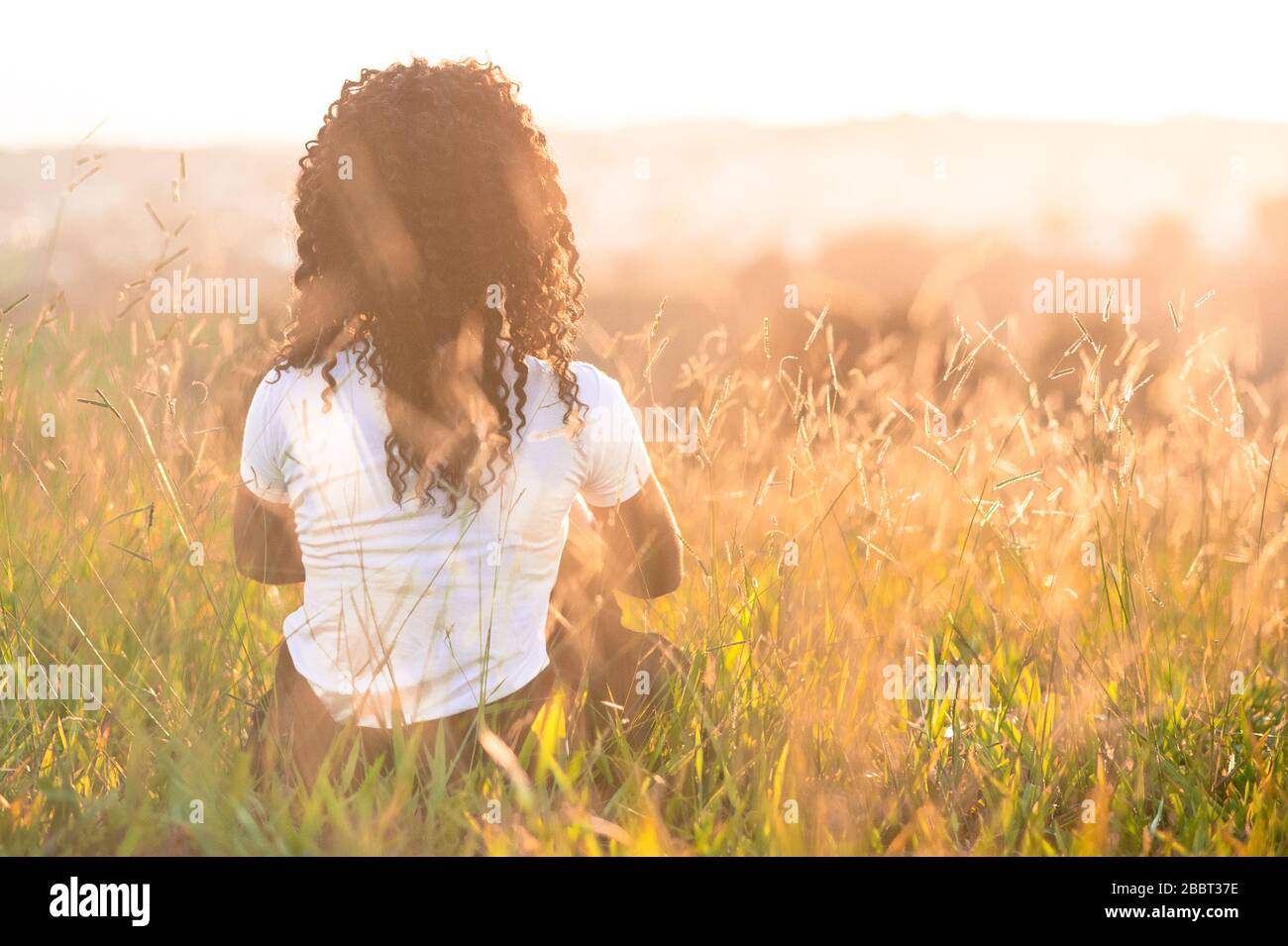 afro american girl on her back sitting in the field at sunset Stock ...