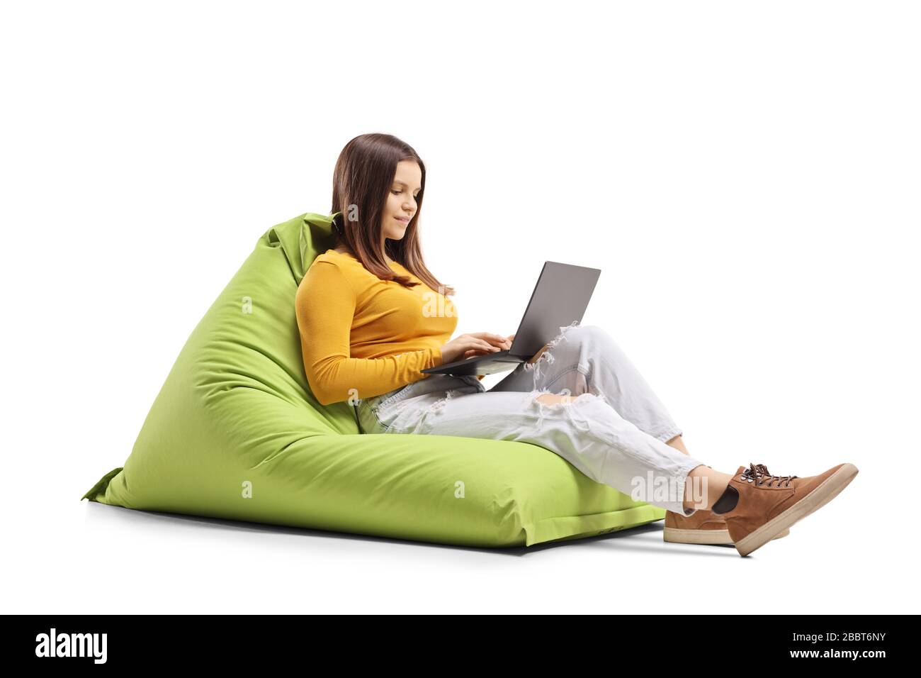 Young female sitting on a bean bag chair and using a laptop isolated on ...