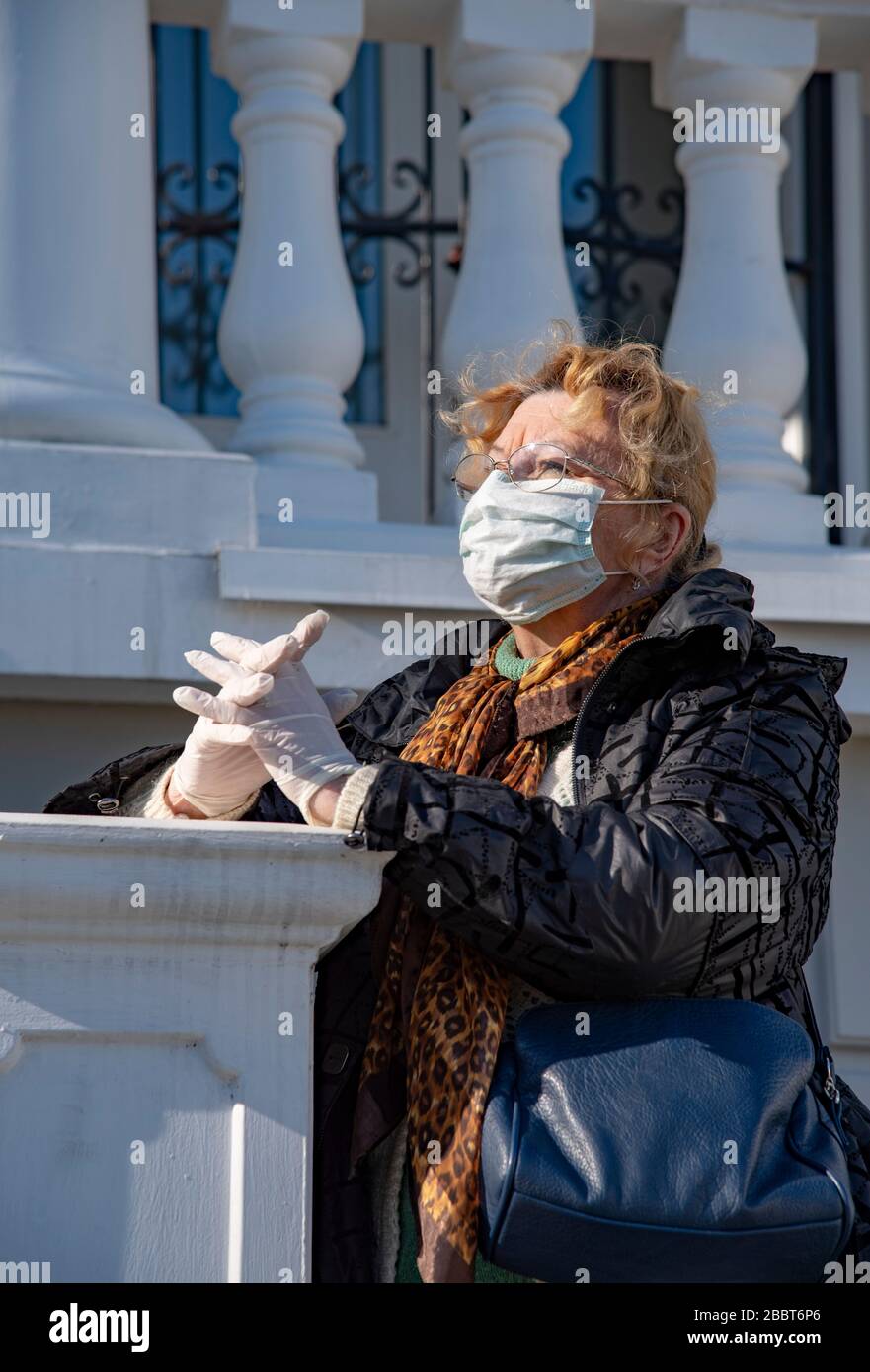 An elderly woman in rubber gloves and a protective mask stands against ...