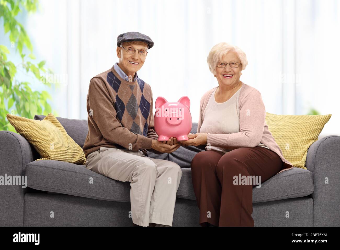 Elderly couple sitting on a sofa at home and holding a piggy bank ...