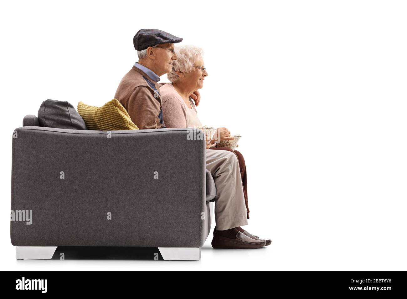 Profile shot of a senior man and woman sitting on a sofa and eating popcorn isolated on white background Stock Photo