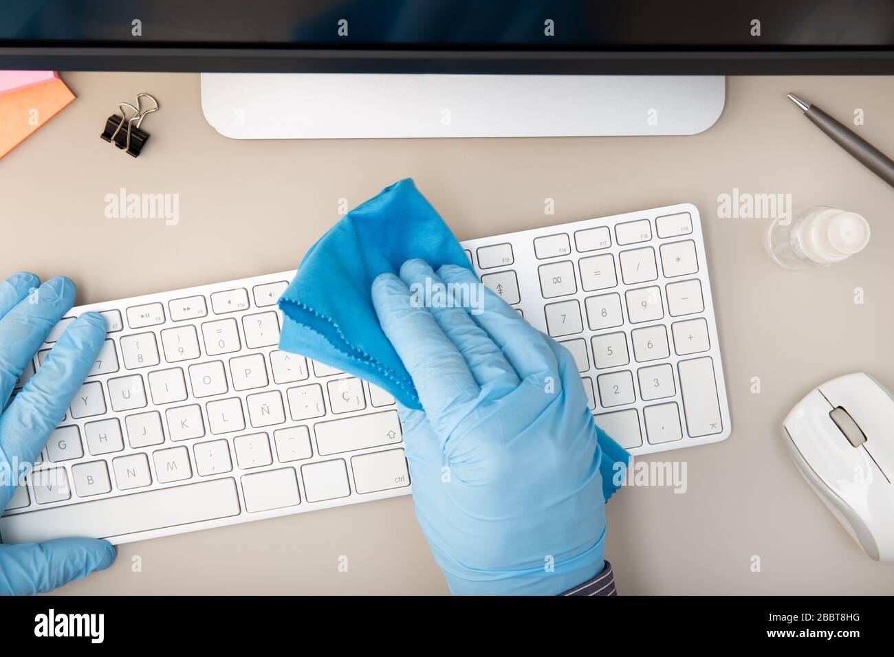 Hand with protective glove cleaning a keyboard with disinfectant. COVID-19 Coronavirus outbreak prevention concept. Top view Stock Photo