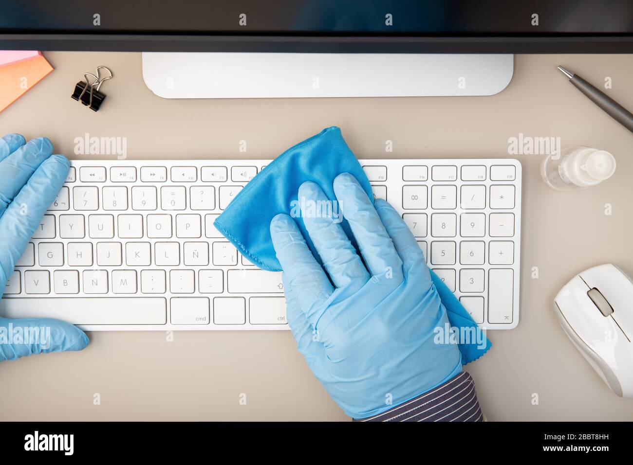 Hand with protective glove cleaning a keyboard with disinfectant. COVID-19 Coronavirus outbreak prevention concept. Top view Stock Photo