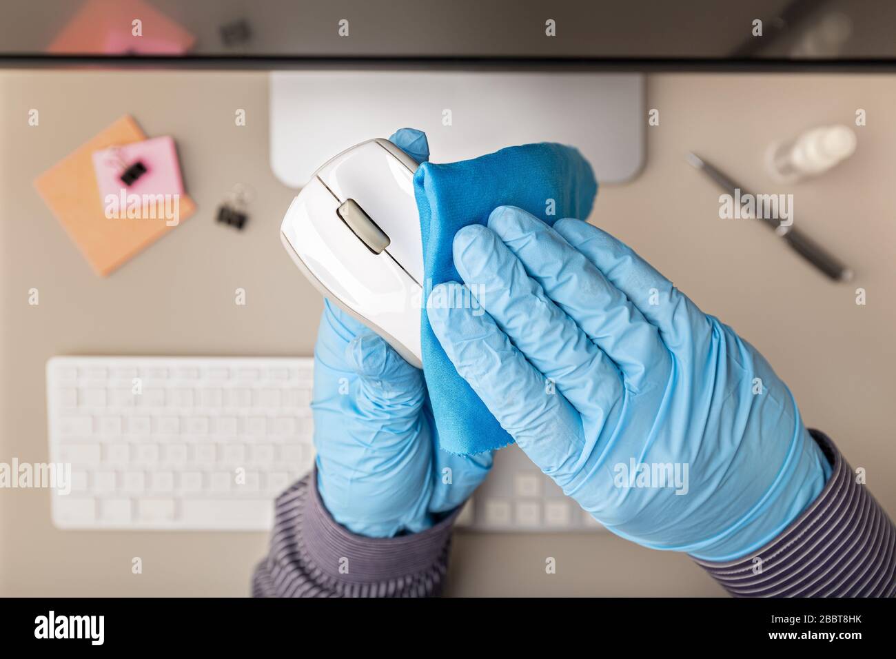 Hand with protective glove cleaning a computer mouse with disinfectant. COVID-19 Coronavirus outbreak prevention concept. Top view Stock Photo