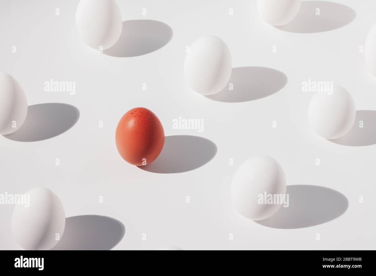 one brown egg among several white eggs on a white background, isometric composition Stock Photo