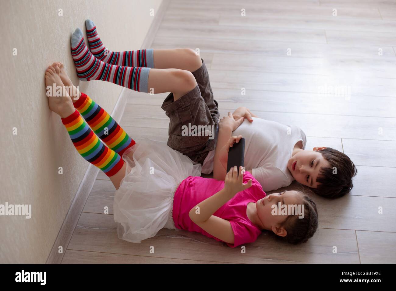 Two children, brother and sister, are lying on the floor with their legs in  bright striped leggings on the wall and playing on a smartphone. Stay home  Stock Photo - Alamy
