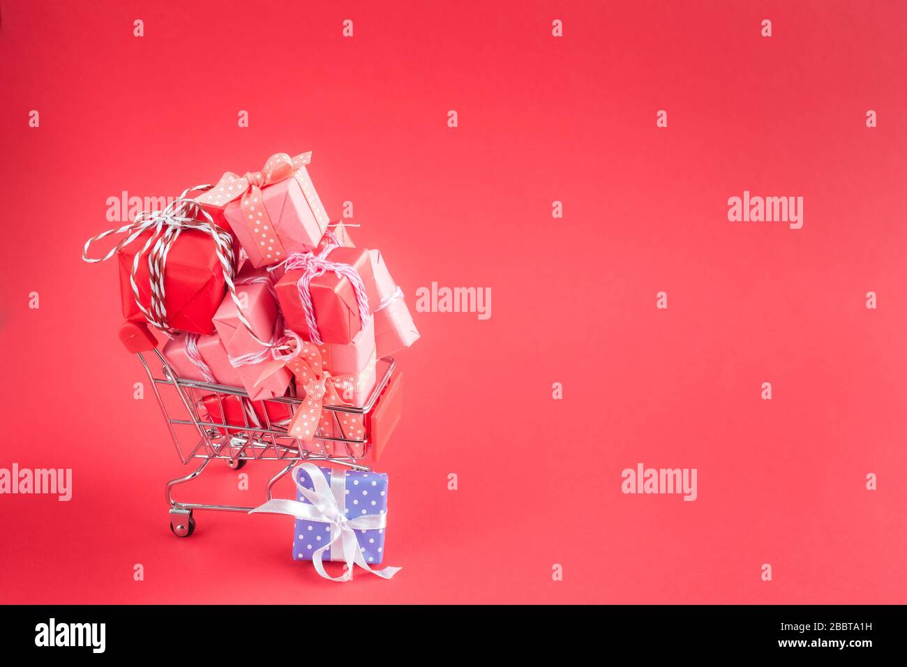 Trolley shopping cart filled with a lot of paper wrapped gift boxes on red background. Concept of online shopping. CopySpace for text. Stock Photo