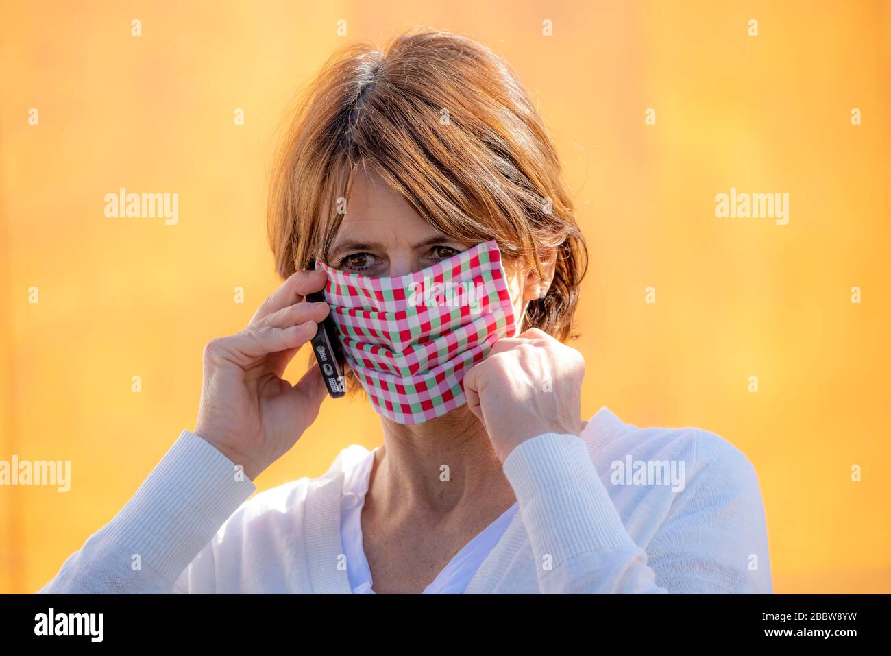 Woman wears a breathing mask, self-sewn, made of cotton, talks on a mobile phone, effects of the corona crisis in Germany Stock Photo