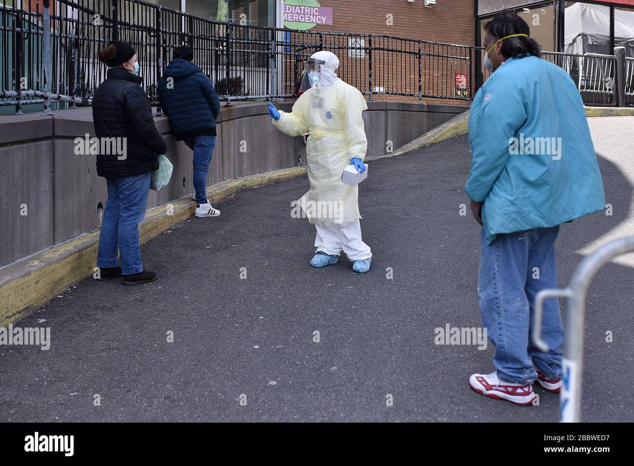 New York City, USA. 01st Apr, 2020. A frontline healthcare worker (center) in protective gown, mask, face shield and gloves talks to a woman who stands in line COVID-19 testing at Elmhurst Hospital Center in the New York City borough of Queens, New York, April 1, 2020. Frontline medical workers still wait for the patients needing testing as the death toll from the coronovirus passes 1000 as of March 31, 2020. (Anthony Behar/Sipa USA) Credit: Sipa USA/Alamy Live News Stock Photo