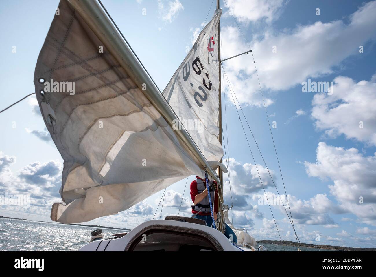 Sailor reefing the main sail doing a solo trip on a sailing boat Stock Photo