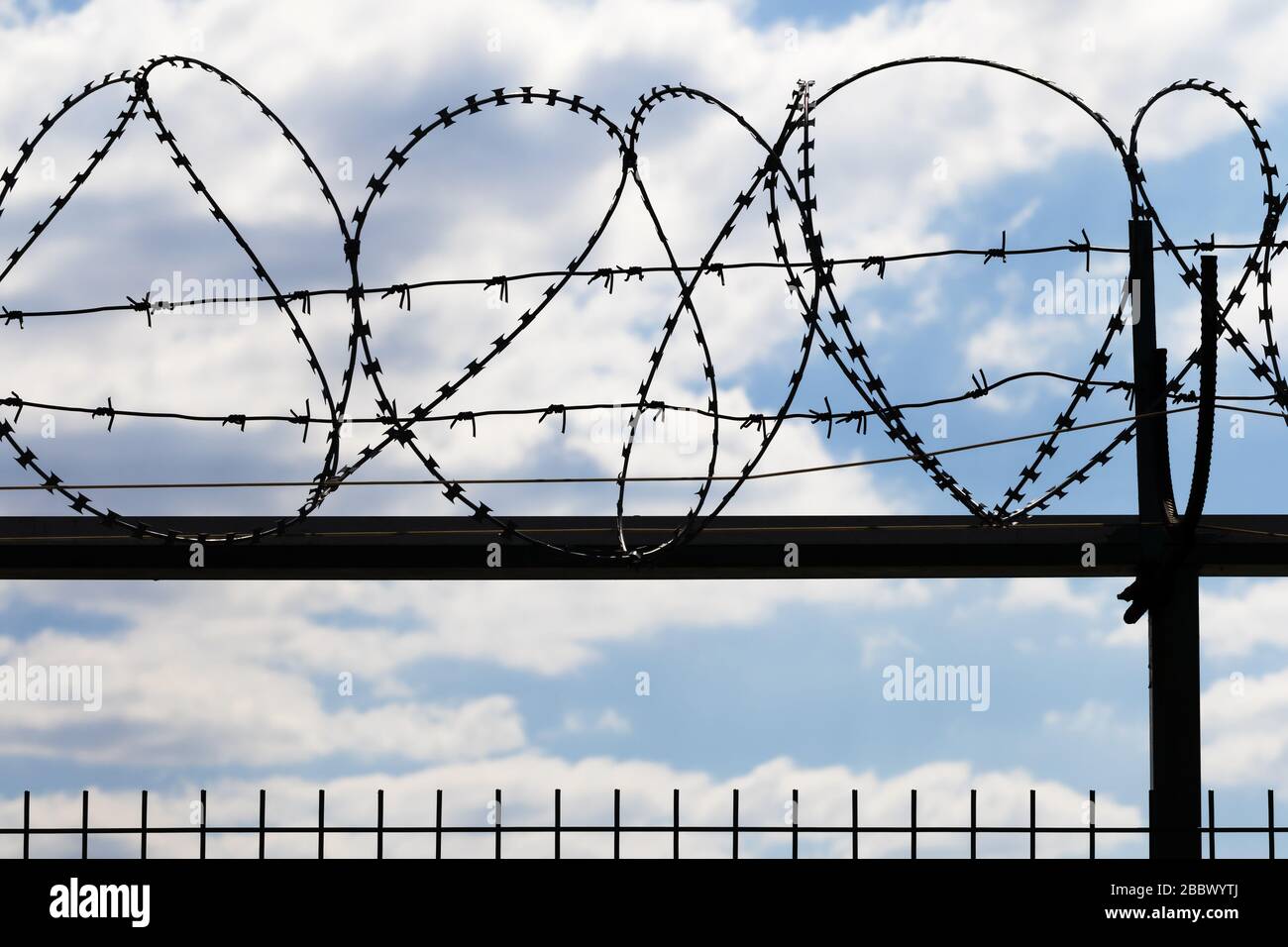 Black coiled barbed wire fence and blue sky with sunlit clouds at ...