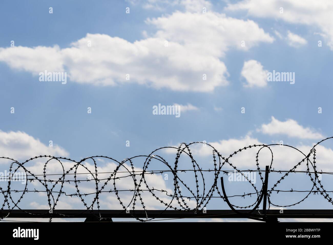 Black coiled barbed wire fence and blue sky with sunlit clouds at ...
