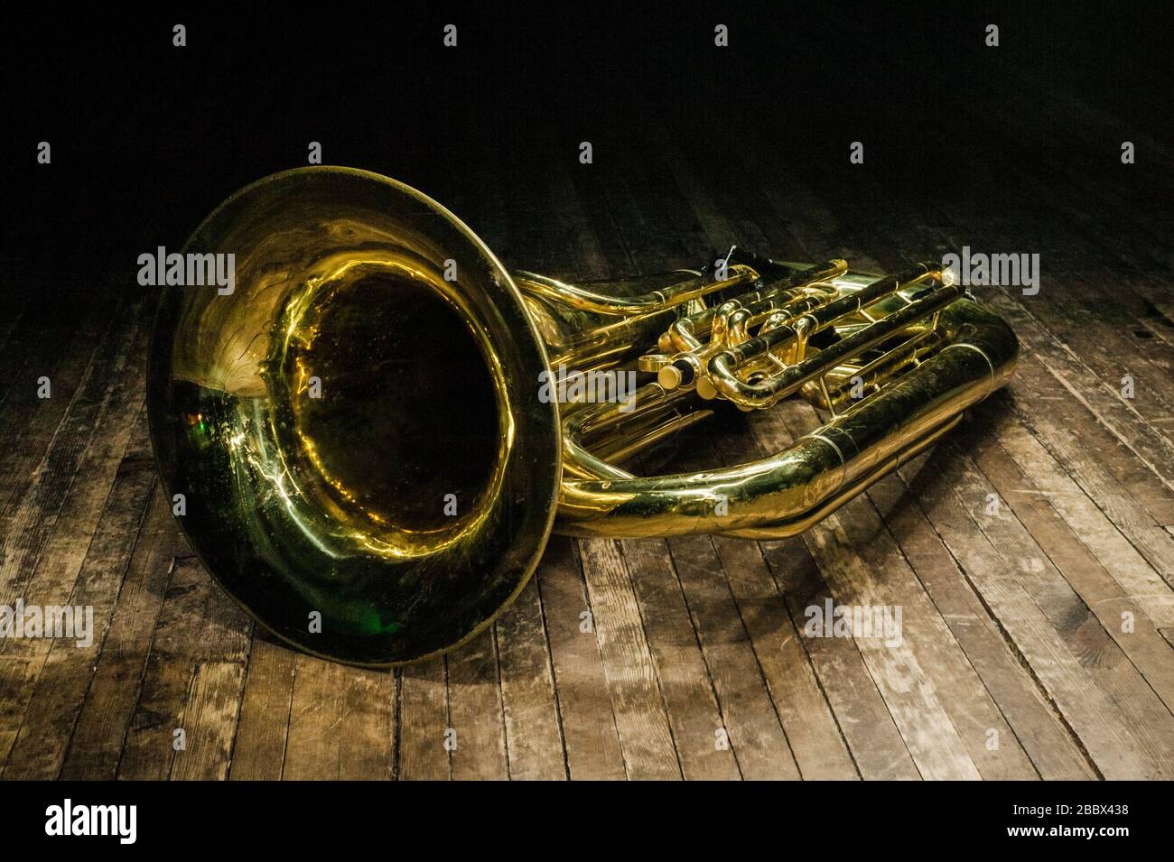 golden brass instrument tuba lies on a brown wooden stage in the light