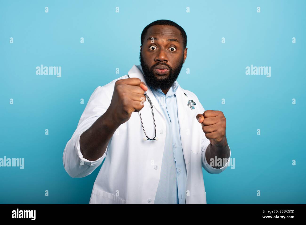 Worried medic is attacked by covid-19 coronavirus. Blue background Stock Photo