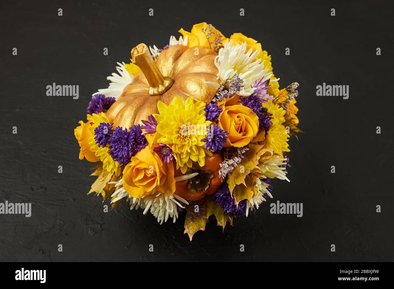 Small pumpkin decorated with yellow and blue flowers as a gift on a black background. Stock Photo